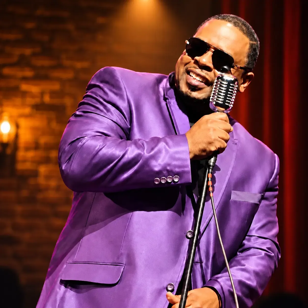Shawn Cornelius in a purple suit singing into a vintage microphone under warm light